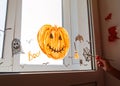 Child painting pumpkin on window preparing celebrate Halloween. Little kid draws decorates room interior with paper bats