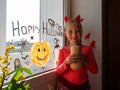 Child painting pumpkin on window preparing celebrate Halloween. Little kid draws decorates room interior with paper bats