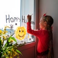 Child painting pumpkin on window preparing celebrate Halloween. Little kid draws decorates room interior with paper bats