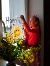 Child painting pumpkin on window preparing celebrate Halloween. Little kid draws decorates room interior with paper bats