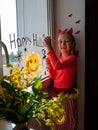 Child painting pumpkin on window preparing celebrate Halloween. Little kid draws decorates room interior with paper bats