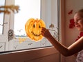 Child painting pumpkin on window preparing to celebrate Halloween. Little girl decorates her room autumn holiday at home Royalty Free Stock Photo