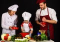 Child with parents cooking at kitchen. Happy family in chef uniform preparing dinner together. Royalty Free Stock Photo