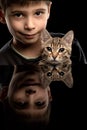 Child with a pet. A boy with a kitten on a black background is reflected in the mirror