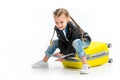 Child with pigtails sitting on lying wheel suitcase