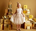 Child among 2 piles of golden gifts in front of plain wall