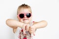 Child in pink sunglasses making funny face. positive girl thumbs down on a white background Royalty Free Stock Photo