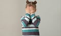 Child placing hands across face to express embarrassment dismay or fear on grey background