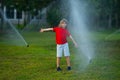 Child play near automatic sprayers in the garden. Watering in the garden. Kid freshness of nature. Automatic lawn