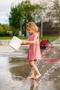 Child playing with bucket at splash pad playground in water park. Girl near fountains in summertime