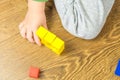 Child is playing with multicolored cubes on wooden floor