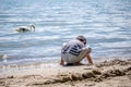 Child playing sands on the beach while swan swimming in water. One little Asian boy in casual clothing with cygnus olor in Royalty Free Stock Photo