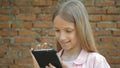 Child Playing Tablet by Bricks Wall in Yard, Little Girl Uses Smartphone Outdoor Royalty Free Stock Photo