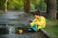 Child playing with toy boat in puddle. Kid play outdoor by rain. Fall rainy weather outdoors activity for young children. Kid Royalty Free Stock Photo