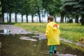 Little boy playing in rainy summer park. Child with umbrella, waterproof coat and boots jumping in puddle and mud in the rain. Kid Royalty Free Stock Photo