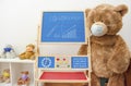 A child playroom or kindergarten with a giant teddy bear wearing medical mask and the growing graph of COVID-2019 cases drawn with