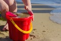 The child plays with a bucket and sand on the seashore in summer day