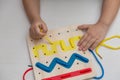 Child plays educational game interestedly with wooden colorful board and laces. Development, education. Royalty Free Stock Photo