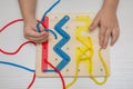 Child plays educational game interestedly with wooden colorful board and laces. Development, education. Royalty Free Stock Photo