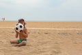 The child plays football on the beach.