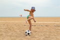 The child plays football on the beach.