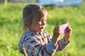 Child plays photographer outdoors. Girl imagines taking pictures on pink plastic toy phone Royalty Free Stock Photo