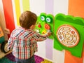 The child plays in the playroom. Happy little kid boy playing on view of colorful plastic playground. Adorable child having fun