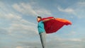 Child plays in red coat, dream of becoming a hero Superwoman. beautiful girl superhero standing on the field in a red