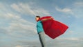 Child plays in red coat, dream of becoming a hero Superwoman. beautiful girl superhero standing on the field in a red