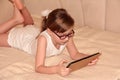 The child plays on the tablet lying on the bed