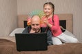 A child prevents a man from working on a laptop in his bedroom. The daughter puts the slinky toy to the father`s head. Family is Royalty Free Stock Photo