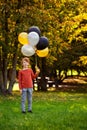 A child of primary school age with balloons in an autumn sunny park. A red-haired boy with a bunch of multicolored gold, black,