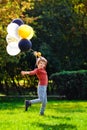 A child of primary school age with balloons in an autumn sunny park. A red-haired boy with a bunch of multicolored gold, black,