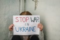 Child protesting war conflict raises banner with inscription Stop war in Ukraine. Kid sits near old broken wall and calls No War.