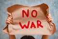 child raises a banner with the inscription no war, standing on the gray concrete background of the studio.