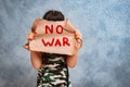 child raises a banner with the inscription no war, standing on the gray concrete background of the studio.