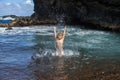 Child raises her hands up in the water and splashes water drops on sea. Kids summer vacation and travel concept.