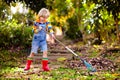 Child and rake in autumn garden. Kid raking leaves Royalty Free Stock Photo