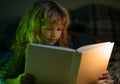 Child read fairy tale from book. Child little boy reading a book in the dark home. Kids face with night light. Royalty Free Stock Photo