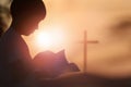 A child reading a bible and a cross in the sunset sky Royalty Free Stock Photo