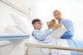 Child reading a book and lying in bed in hospital room with a nurse holding a teddy bear sitting beside him Royalty Free Stock Photo