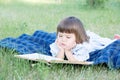 Child reading book lying on stomach outdoor, smiling cute little girl, children education and development Royalty Free Stock Photo