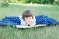 Child reading book lying on stomach outdoor, smiling cute little girl, children education and development Royalty Free Stock Photo