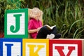 Child reading book in school yard. Kid learning abc letters. Little boy sitting on wooden toy blocks with alphabet in preschool or Royalty Free Stock Photo