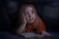 Child reading a book under the covers. Immersion into the magical world Royalty Free Stock Photo