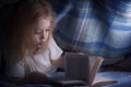 Child reading a book under the covers. Immersion into the magical world Royalty Free Stock Photo