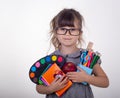 Child ready for school. Cute clever child in eyeglasses holding school supplies: pens, notebooks, scissors and apple.