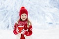 Child in red hat drinking hot chocolate in snow on Christmas vacation. Winter outdoor fun. Kids play in snowy park on Xmas eve.