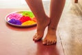 Child rests her legs on the floor beside a plate filled with holi powders