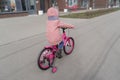 A child rides a bicycle in a pink jacket. A child with his back to the photographer. Spring walks near the house on the